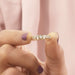 A Women Holding Baguette And Round Cut Diamond Bezel Set Wedding Band between two fingers and the background is soft pink.